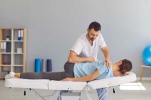 A chiropractor gently adjusting the back of an adult patient lying face down in a softly lit clinic room.