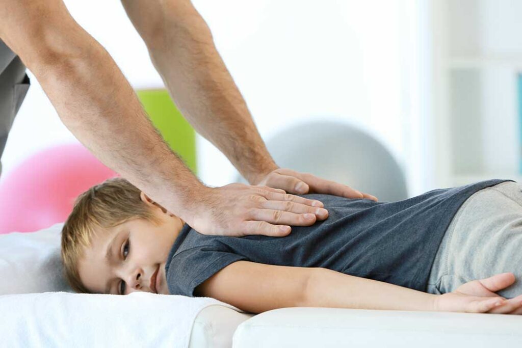 Person receiving a gentle spinal adjustment on a padded treatment table while discussing back stiffness.